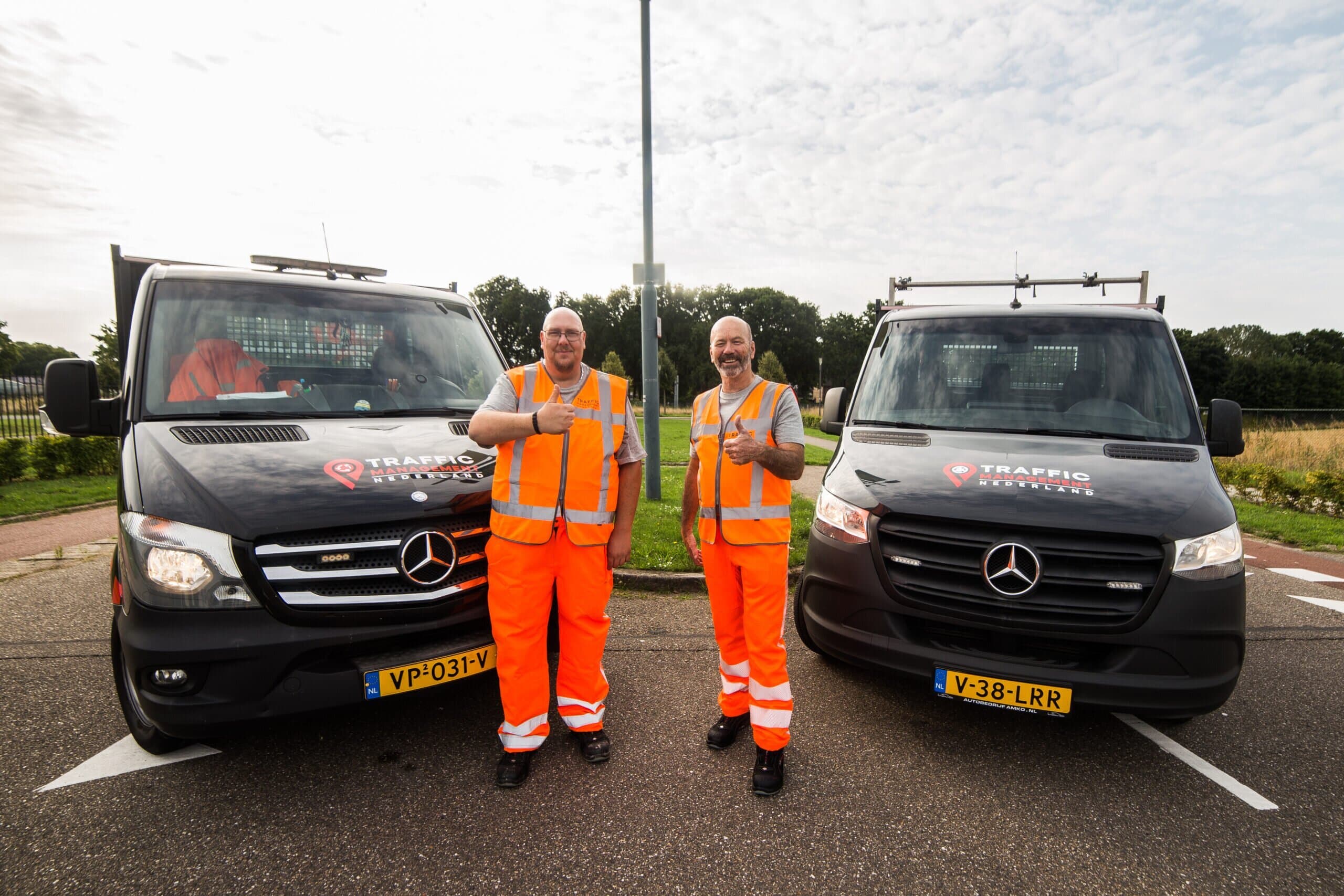 Twee teamleden van een traffic management bedrijf bij twee bedrijfsbusjes, klaar voor werkzaamheden.